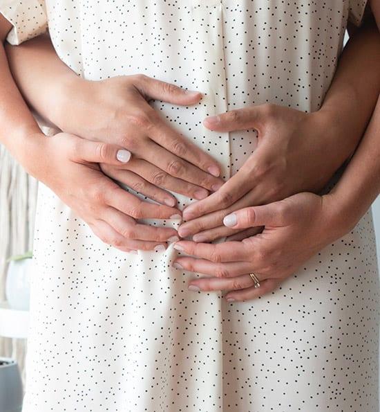 Pregnant lady with partner's hands around stomach